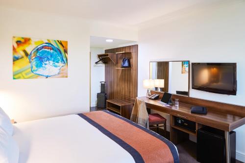 a hotel room with a bed and a desk and a tv at Mercure St Helens in Saint Helens