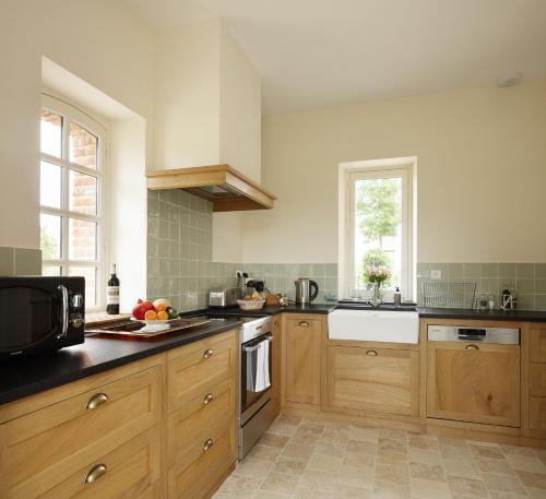 a kitchen with wooden cabinets and a microwave at Le Domaine de Ravenoville - Pierres d'Histoire in Ravenoville