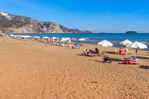a beach with umbrellas and people sitting on the sand at Kalamaki Beach Hotel, Zakynthos Island in Kalamaki