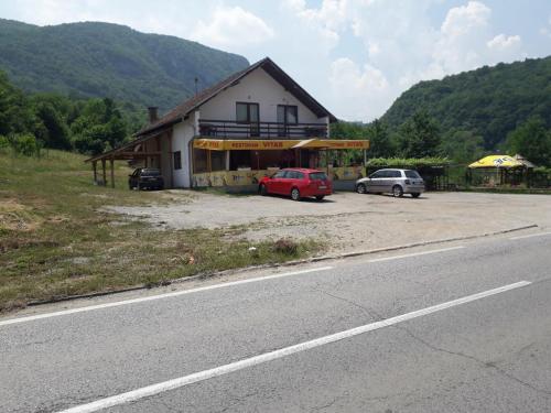 a house with two cars parked next to a road at Prenoćište Vitas in Miljevina