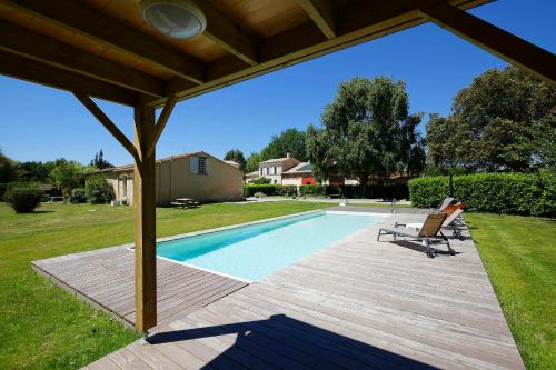 a swimming pool with a wooden deck next to a house at Domaine de Ludeye in Listrac-Médoc