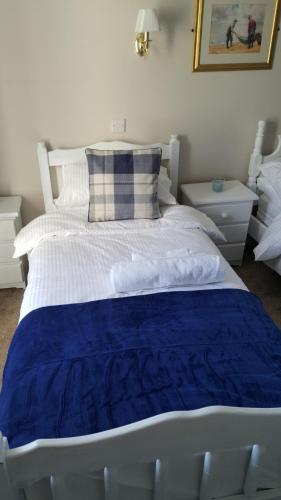 a large white bed with a blue blanket on it at Central Bar Guesthouse in Cushendall