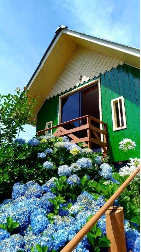 a green house with blue flowers in front of it at Cabanas Costaneira in Cambará