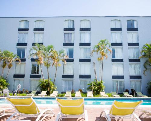 a hotel with chairs and palm trees in front of a pool at Plaza Hotel Fort Lauderdale in Fort Lauderdale