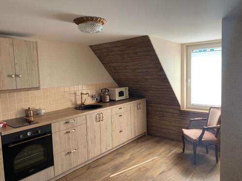 a kitchen with wooden cabinets and a staircase with a window at Arbatinės apartamentai in Biržai