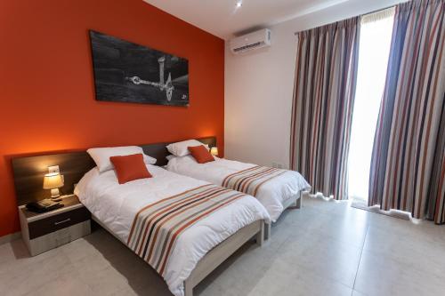 two beds in a hotel room with orange walls at The Shipwright's Lodge in Marsaxlokk