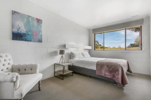 a white bedroom with a bed and a chair at Hybiscus Waterfront Apartments in Lakes Entrance