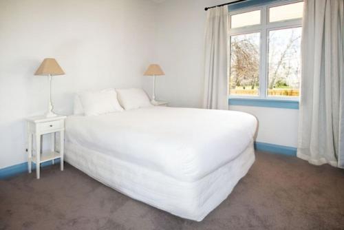 a white bedroom with a large white bed and a window at McDougall Cottage in Wanaka