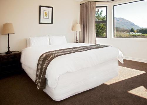 a white bed in a room with a large window at Pembroke Lodge in Wanaka