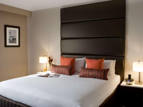 a bedroom with a large white bed with orange pillows at Novotel Sydney International Airport in Sydney