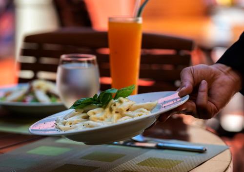 a person holding a plate of pasta on a table at Lancaster Tamar Hotel- Hadath in Beirut