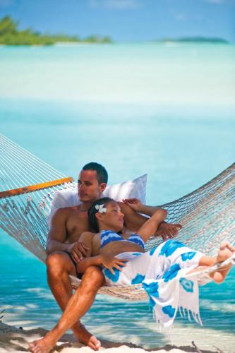 a man and a woman laying on a hammock on the beach at Tamanu Beach in Arutanga
