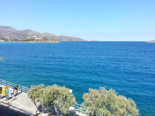 a large body of water with two people walking on a sidewalk at Angelos Hotel in Agios Nikolaos