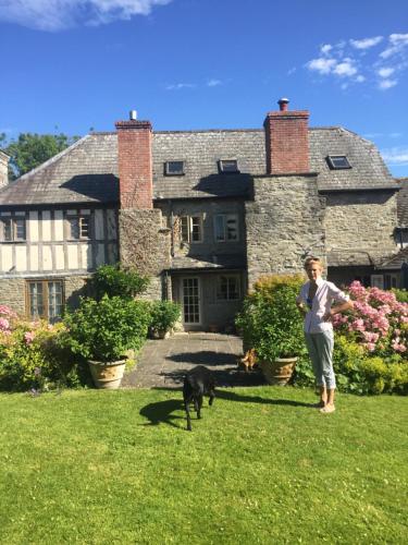Una donna in piedi davanti a una casa con un cane di Lower House Farm B&B, Herefordshire a Hergest
