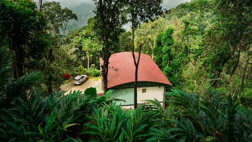 een klein huis met een rood dak in een bos bij Stallion Estates in Munnar