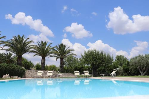 a swimming pool with chairs and a table and palm trees at Tenuta Aguglia in Noto