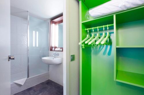 La salle de bains est pourvue de murs verts, d'un lavabo et d'une douche. dans l'établissement Campanile Hôtel Auch, à Auch