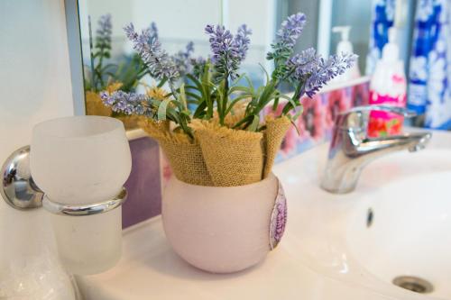 Un jarrón con flores púrpuras sentado en el lavabo del baño en Guests house "Like Home", en Sigulda