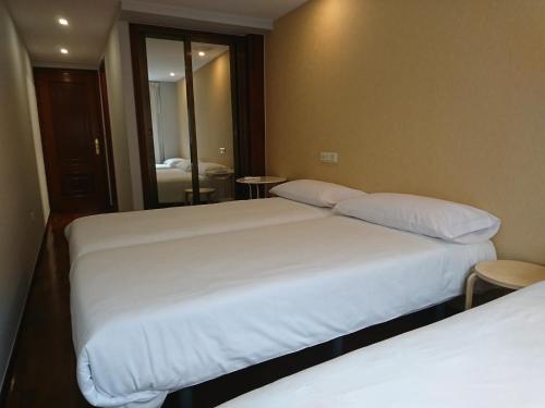 two beds in a hotel room with a mirror at Saudade Hostal Cafetería in A Coruña