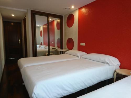 two beds in a hotel room with red walls at Saudade Hostal Cafetería in A Coruña