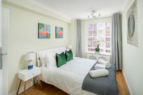 a bedroom with a white bed with green pillows at Homm - Hyde park 2 bedroom flat in London
