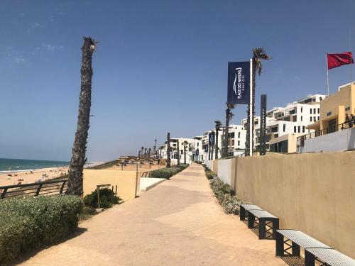 a path leading to a beach with benches and palm trees at Luxury Apartement Near the Beach in Sidi Bouqnadel
