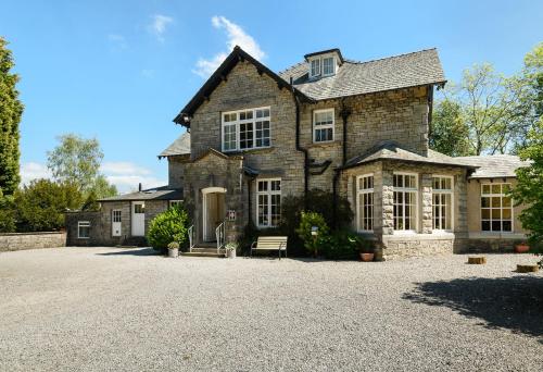a large stone house with a gravel driveway at Woodlands Hotel & Pine Lodges in Grange Over Sands