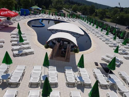 a pool with white chairs and umbrellas at Pensiunea Duet in Sărata-Monteoru