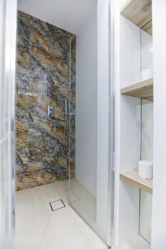 a glass shower in a bathroom with a stone wall at M&K Apartamenty - Morska Bryza, Sobieszewo- Wyspa Sobieszewwska in Gdańsk