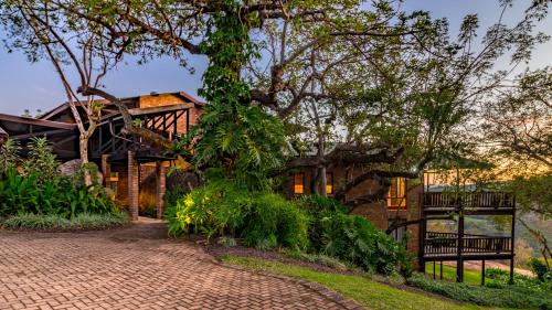 a house with a brick driveway in front of a tree at Ulwazi Rock Lodge in Hazyview