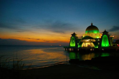 a mosque with green lights on the water at night at Lavender@Guesthouse in Melaka