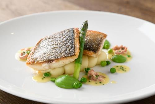 a white plate with a piece of fish and vegetables at The Bell at Ramsbury in Marlborough