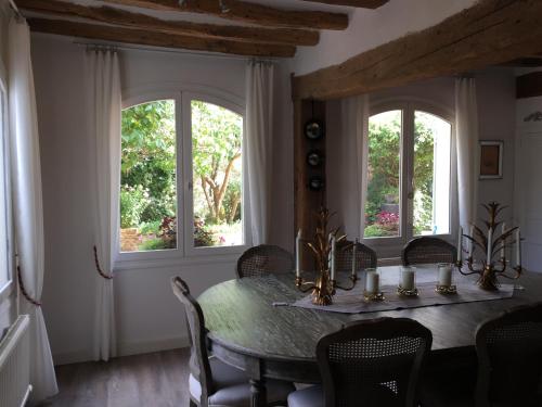 uma sala de jantar com uma mesa e duas janelas em B&B les Agapanthes em Gasny