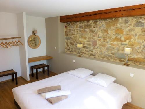 1 dormitorio con cama blanca y pared de piedra en L'Accent d'ici en Le Somail