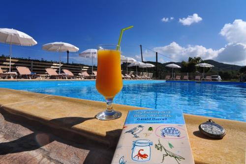 a book and a glass of orange juice next to a pool at Makris Apartments Arillas Corfu in Arillas