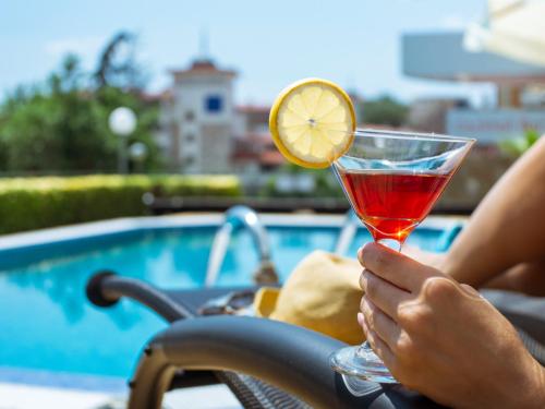 a person holding a drink in front of a pool at Milennia Family Hotel in Sunny Beach