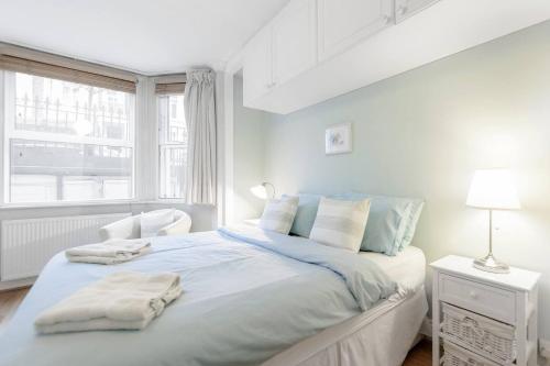 a white bedroom with a bed with blue sheets and a window at 3 Bedroom Garden Flat - Central Location in London