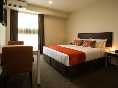a hotel room with a bed, chair, and nightstand at Ramada Suites by Wyndham Christchurch City in Christchurch