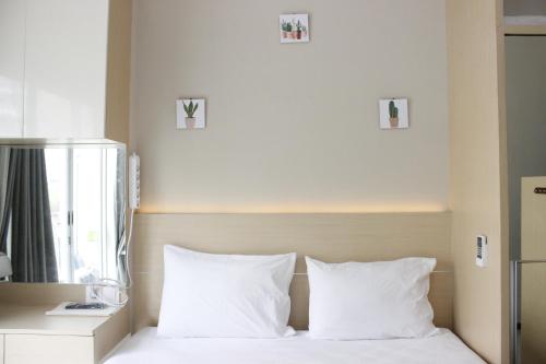 a bed with white pillows and pictures on the wall at Homey Studio Gateway Pasteur Apartment near Exit Toll By Travelio in Bandung