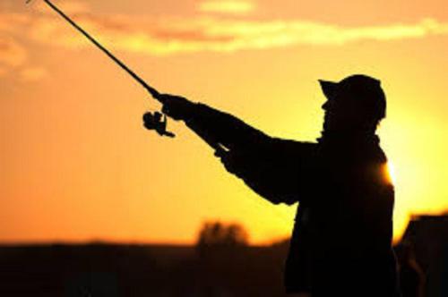 a man is holding a fishing rod at sunset at ALANTOS ŽIRGAI Holiday Villas sauna or hottube additional price in Alanta