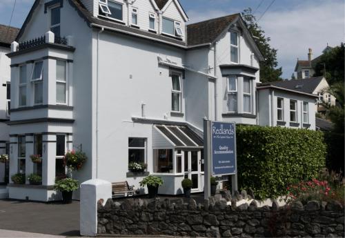 ein weißes Haus mit einem blauen Schild davor in der Unterkunft Redlands in Brixham