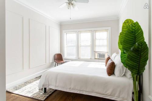 a white bedroom with a large bed and a plant at Lively 2BR Apt in Lincoln Square - Eastwood 47-1 in Chicago