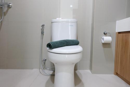 a bathroom with a toilet with a green towel on it at Homey Studio Room Tree Park City BSD Apartment near BSD City By Travelio in Tangerang