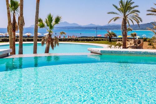 a large swimming pool with palm trees and the ocean at Hotel Club Saraceno - Bovis Hotels in Àrbatax
