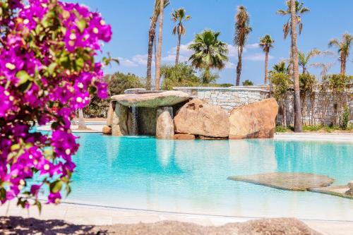 a swimming pool with blue water and purple flowers at Hotel Club Saraceno - Bovis Hotels in Àrbatax