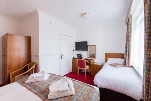 een slaapkamer met 2 bedden en een bureau met een televisie bij The Queens Hotel in Paignton