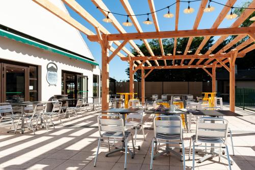 a patio with tables and chairs under a wooden pergola at Campanile Beaune in Beaune