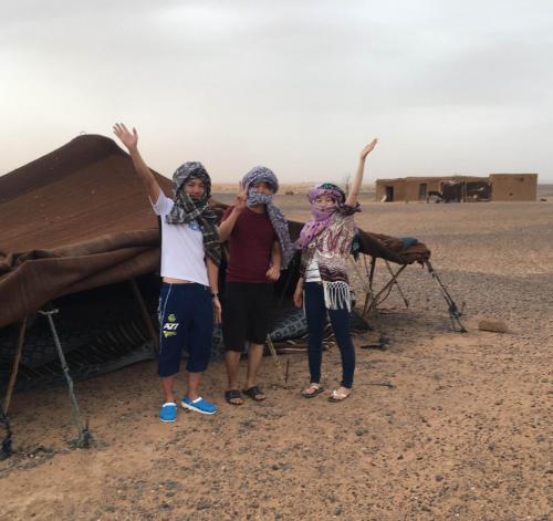 three people standing in front of a tent in the desert at Riad Hotel Les Flamants in Merzouga