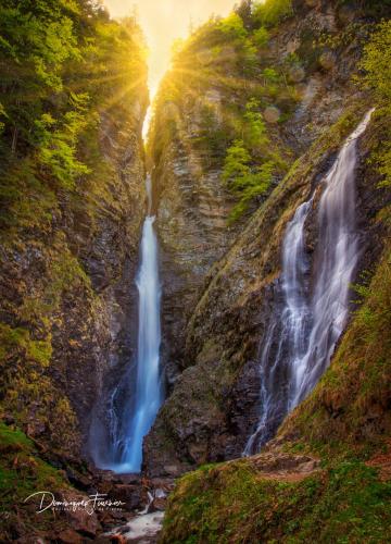 a waterfall on the side of a cliff with the sun setting at hotel des 2 nations in Luchon