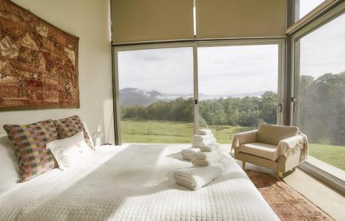 a bedroom with a bed and a chair and a large window at Bundaleer Architect designed stunning views in Kangaroo Valley